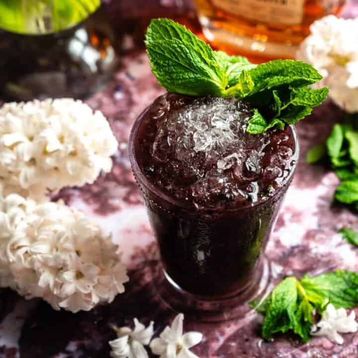 A blueberry lavender mint julep in a glass mint julep cup on a purple marble table.