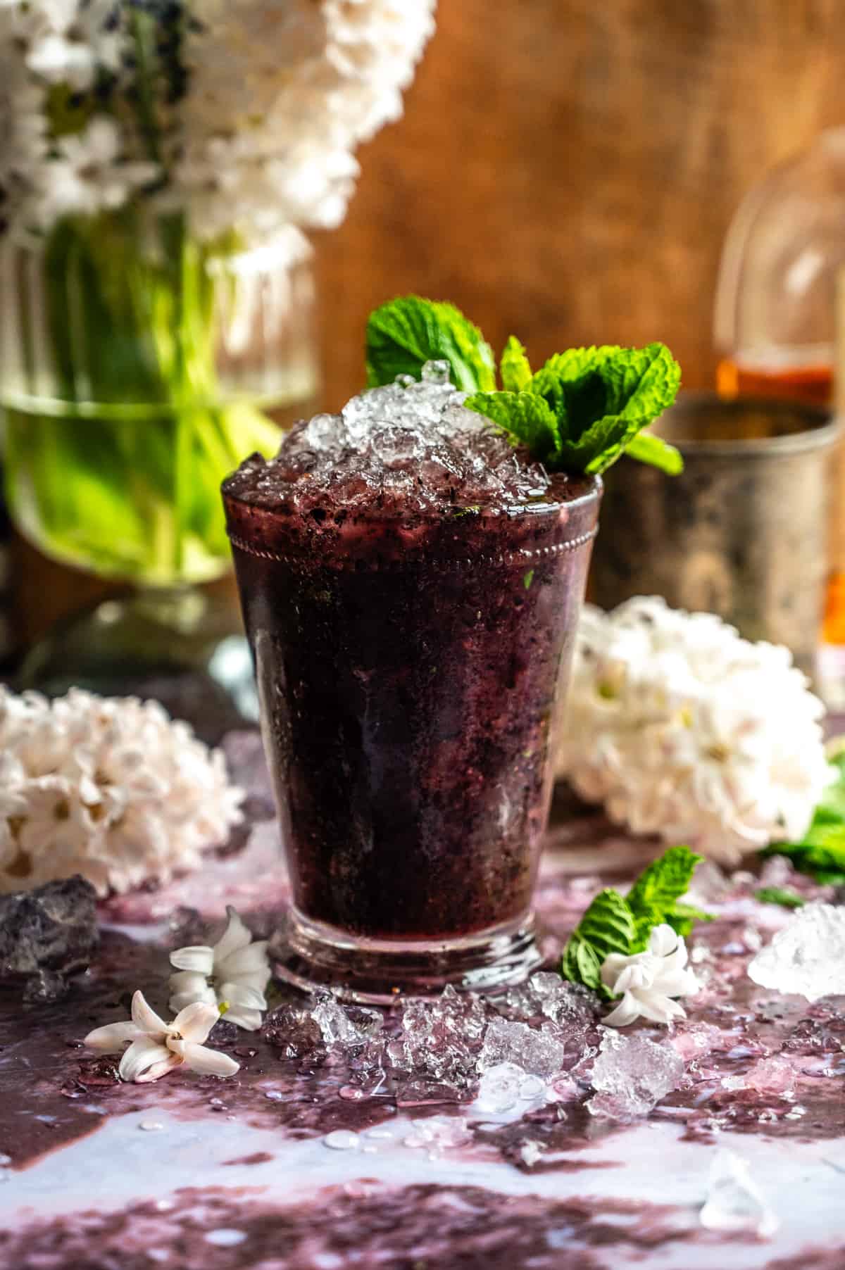 Straight on shot of a blueberry lavender mint julep in a glass mint julep cup on a purple marble table.