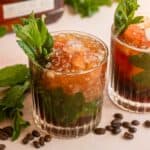 Two rocks glasses filled with the espresso mint julep and garnished with fresh mint on a pink marble table.