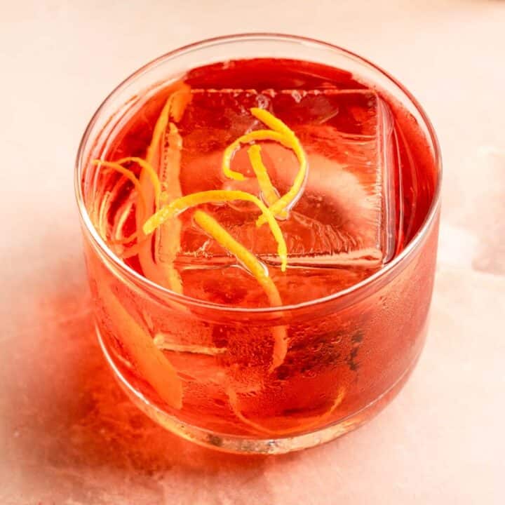 The Boulevardier cocktail on a pink marble table and garnished with orange zest.