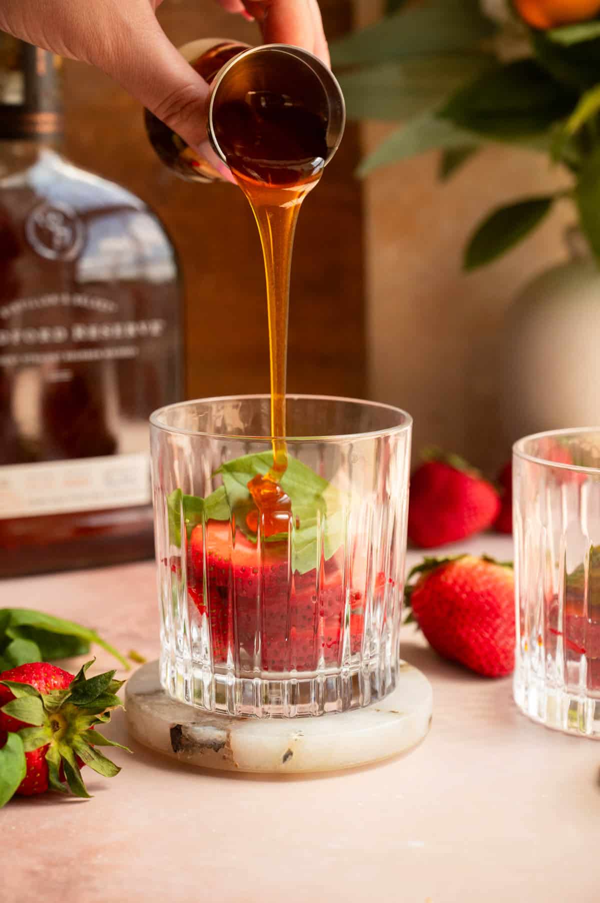 Strawberries and basil in a rocks glass with hot honey being poured over them.