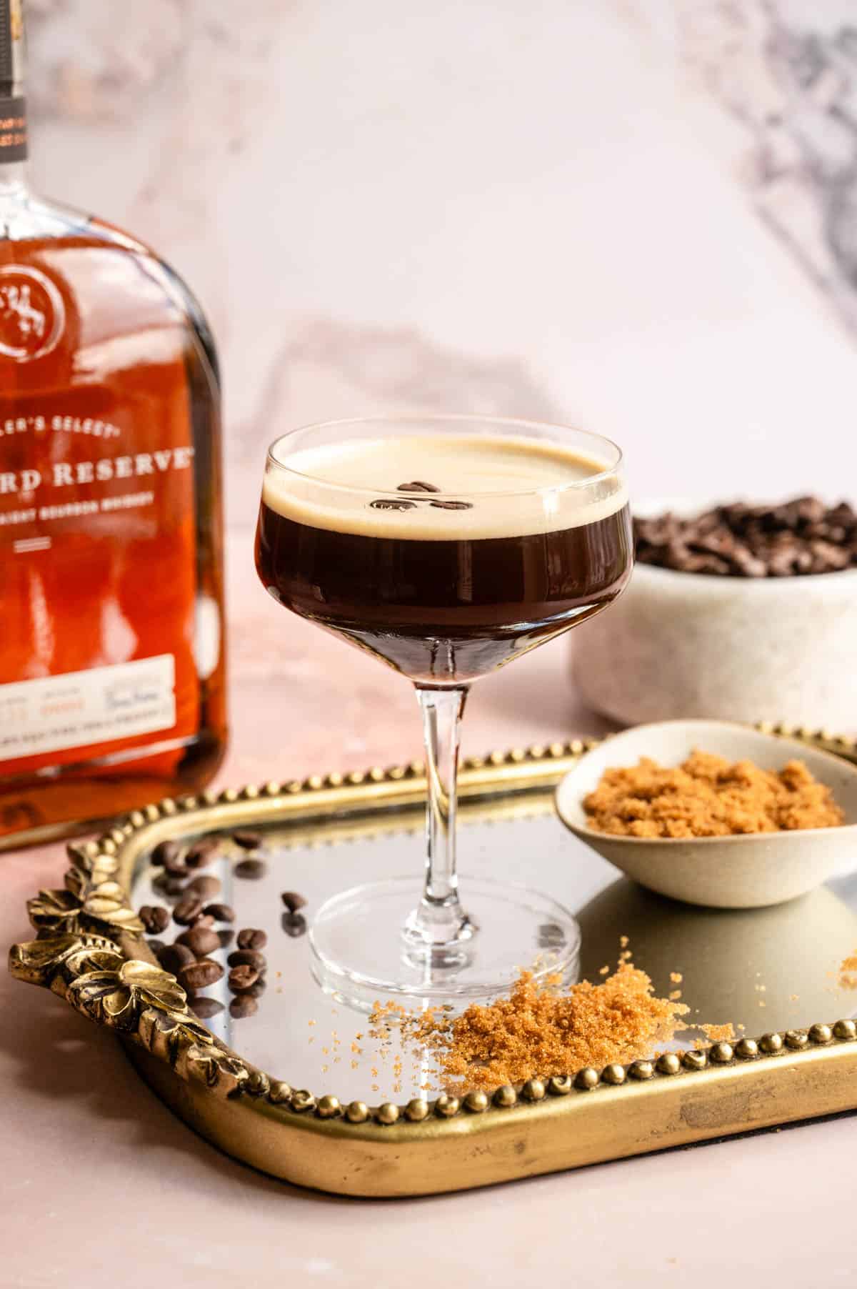 Bourbon Espresso Martini on a mirrored tray with brown sugar, espresso beans, and bourbon around the sides.