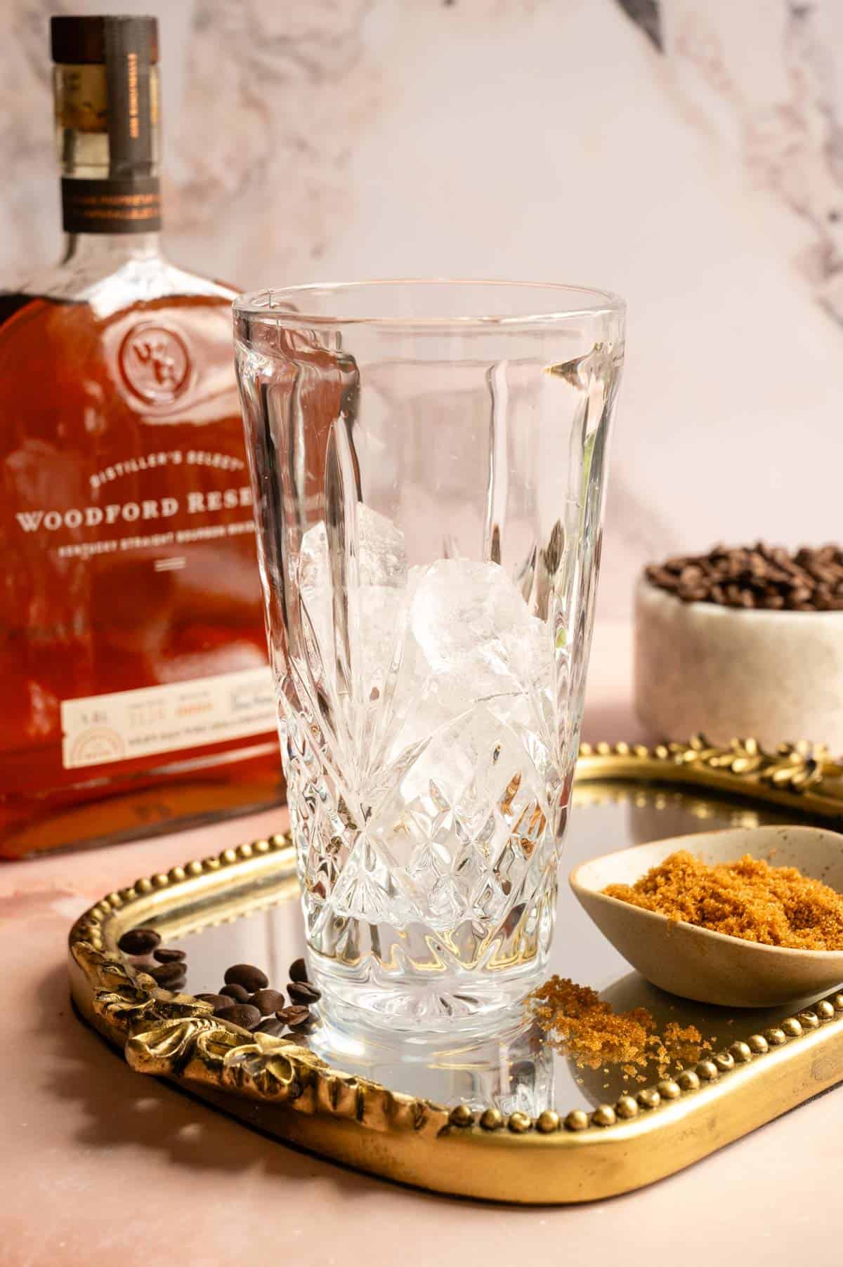 A glass cocktail shake is filled with ice on a mirrored tray.