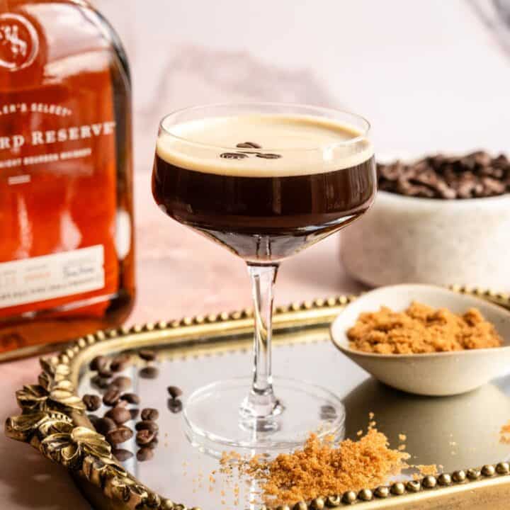 Bourbon Espresso Martini on a mirrored tray with brown sugar, espresso beans, and bourbon around the sides.