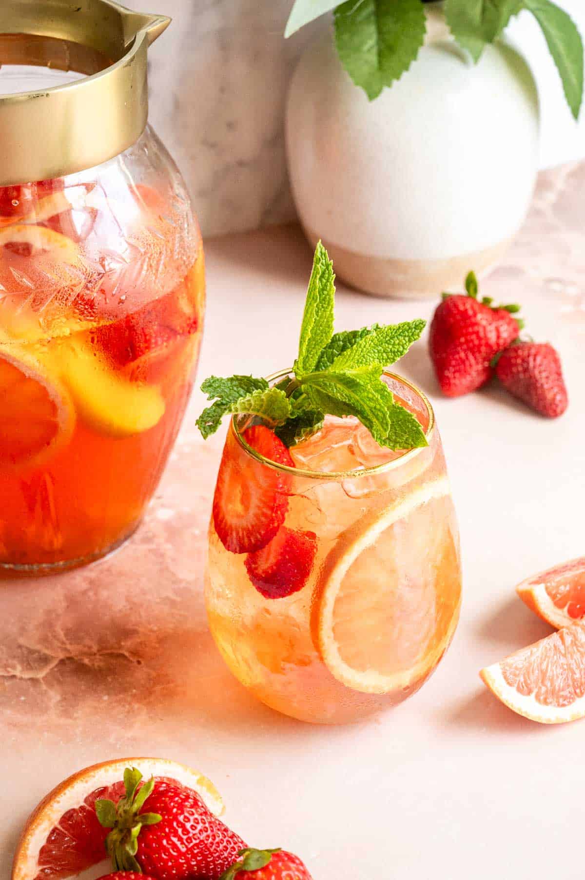 A stemless wine glass on a pink marble table with a pitcher behind it filled with pink sangria.