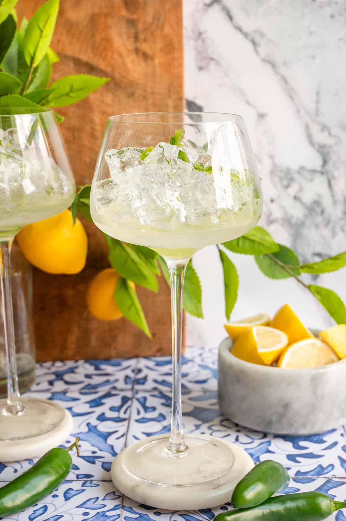 A long stem glass with ice and lemon juice on a blue tile table.