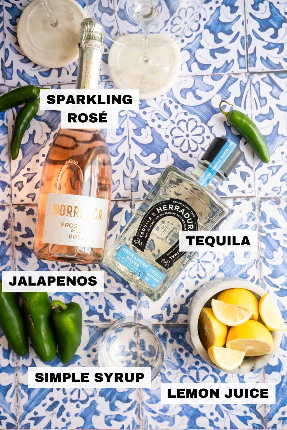 The tequila, rose, sliced lemons, and jalapeños on a blue tile table.