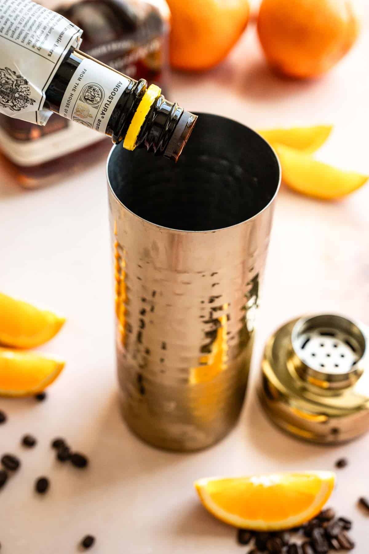 Aromatic bitters being poured into a gold cocktail shaker.