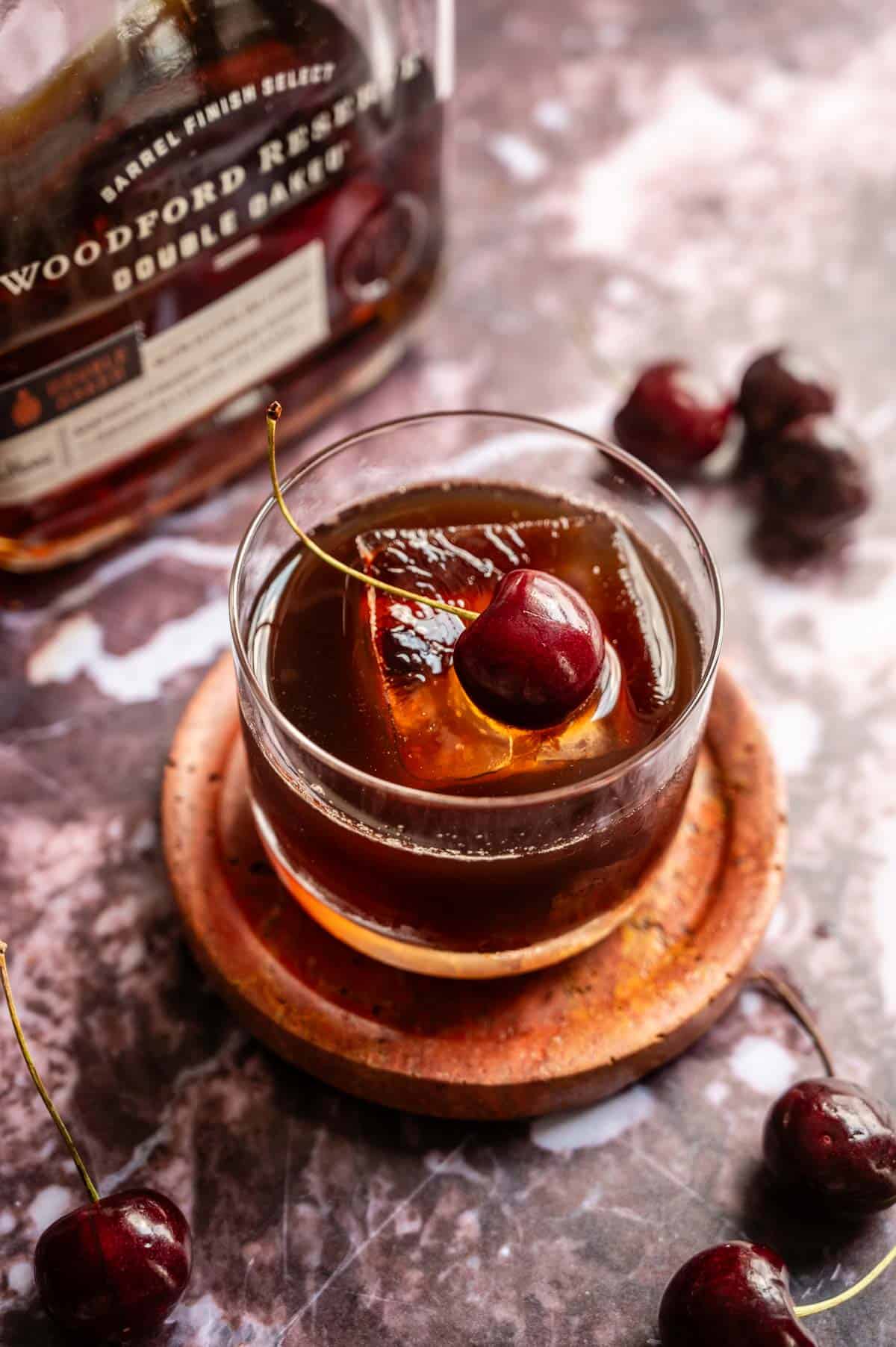 A spiced cherry old fashioned garnished with a single cherry and on a purple marble table.