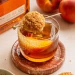 A small rocks glass with the old fashioned and garnished with a small biscuit on a pink marble table.