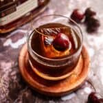 A spiced cherry old fashioned garnished with a single cherry and on a purple marble table.