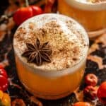 A butterbeer old fashioned garnished with cinnamon dust and star anise on a black and orange marble table.