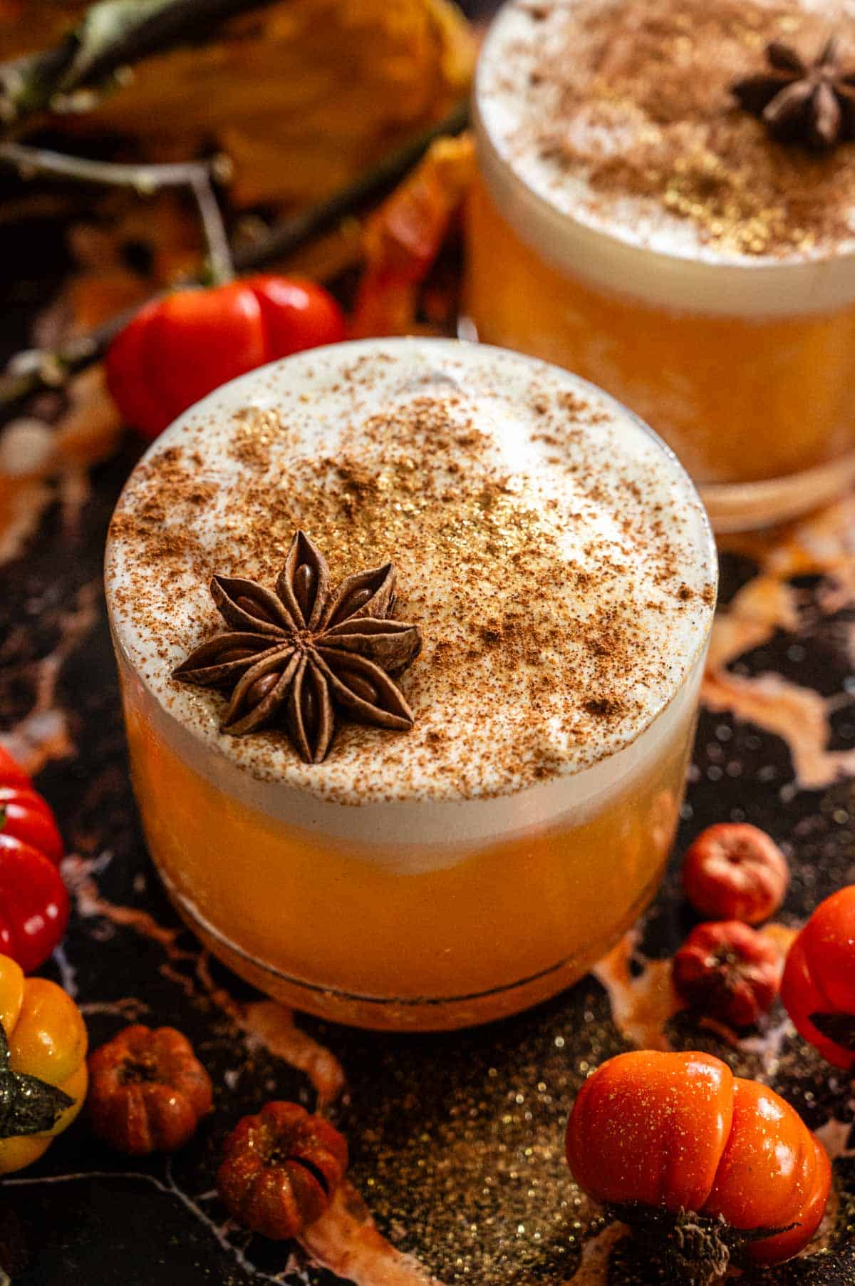 A butterbeer old fashioned garnished with cinnamon dust and star anise on a black and orange marble table.