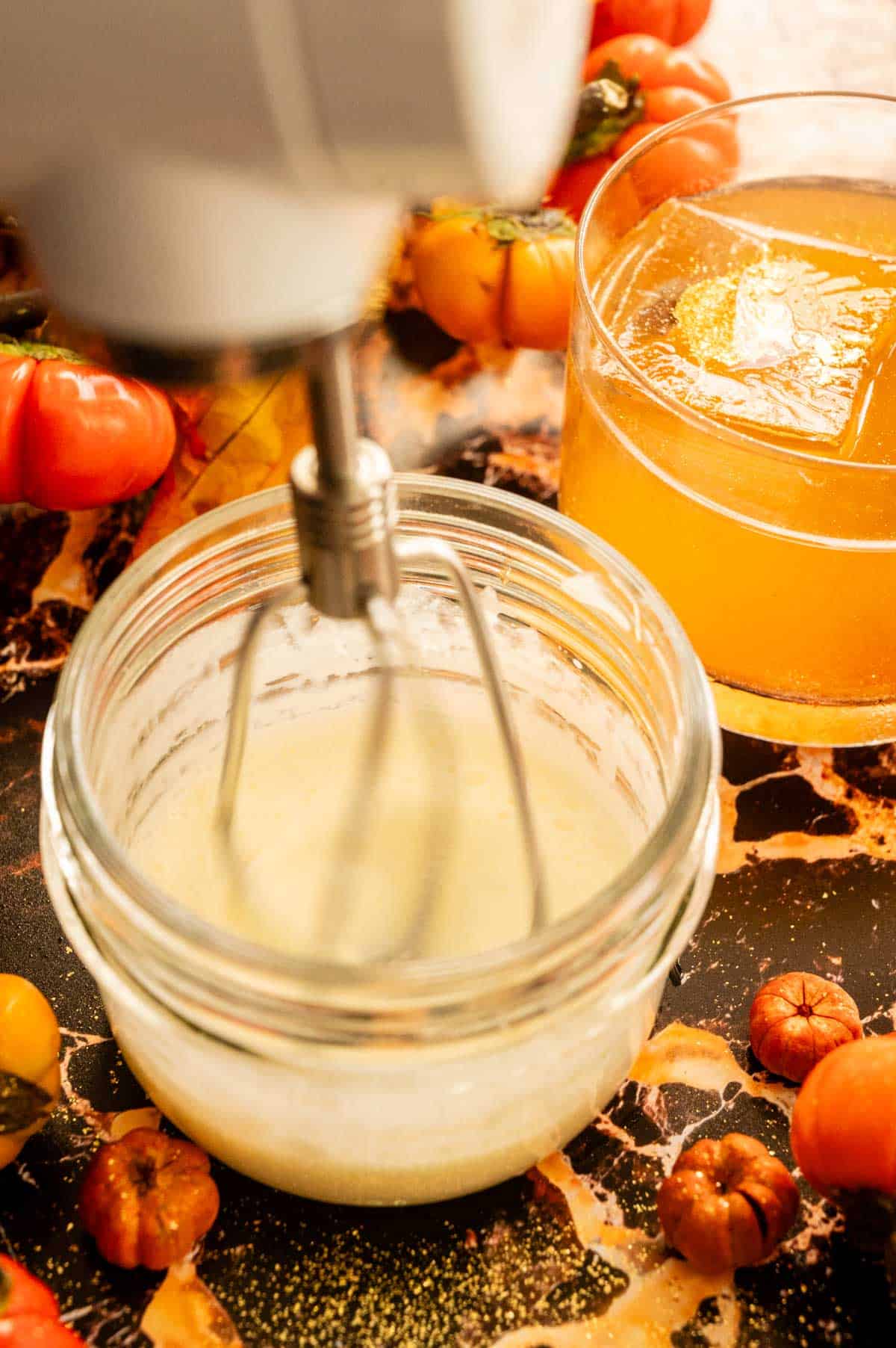 A small mason jar with cream being whipped by a mixer.