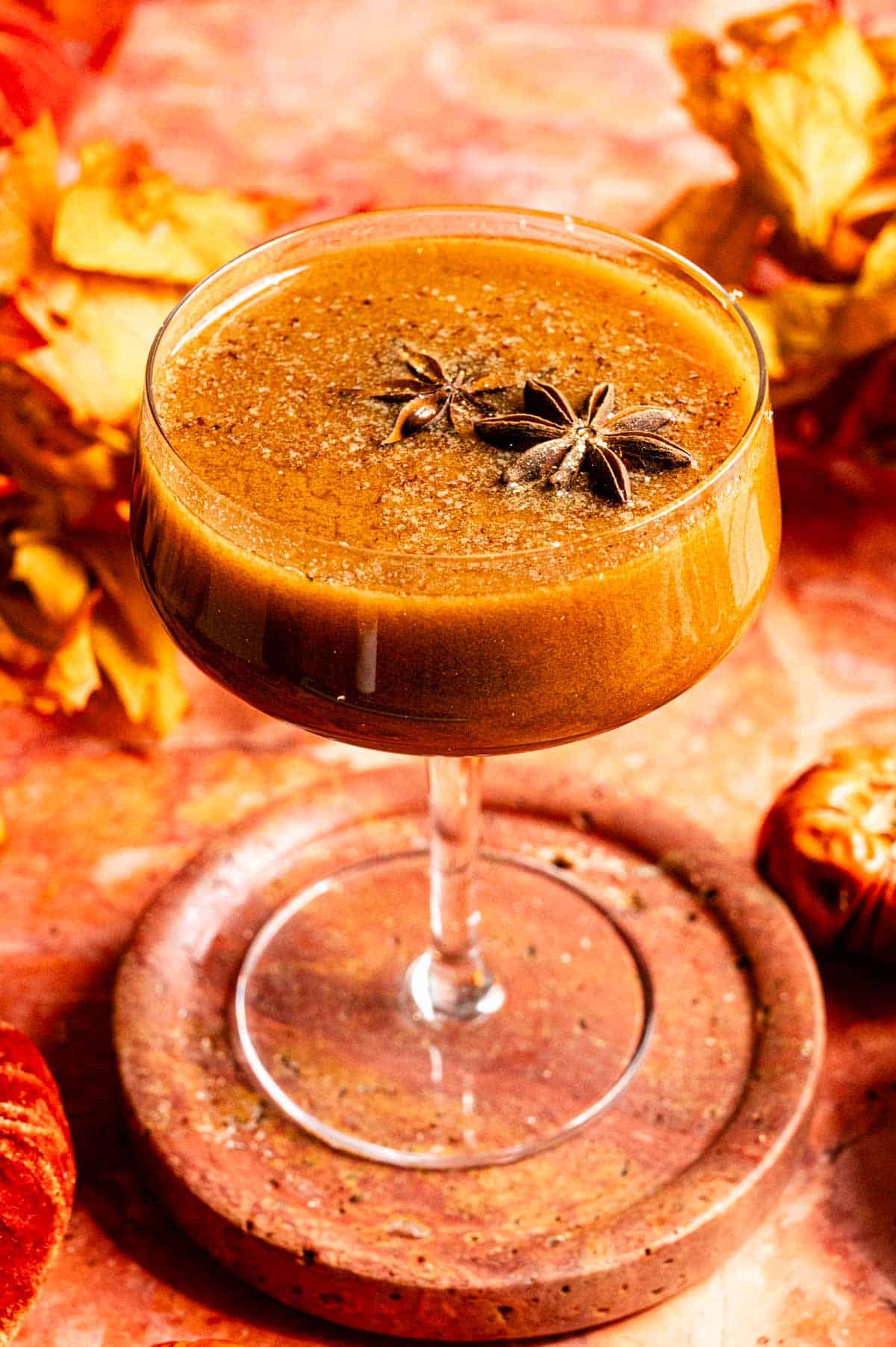 Pumpkin chai Manhattan garnished topped with star anise on a orange marble table.