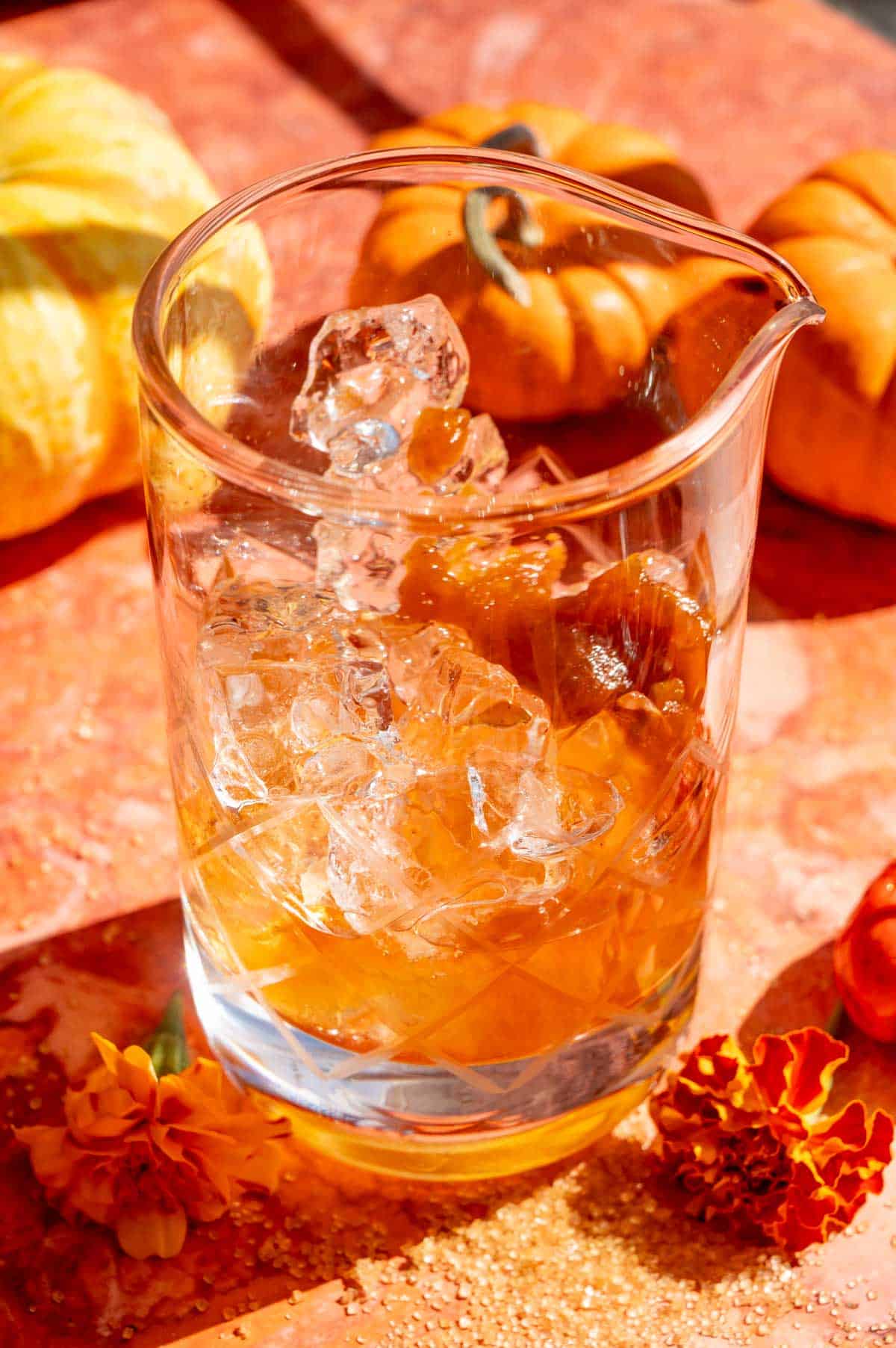 A mixing glass filled with ice, bourbon, and pumpkin butter.