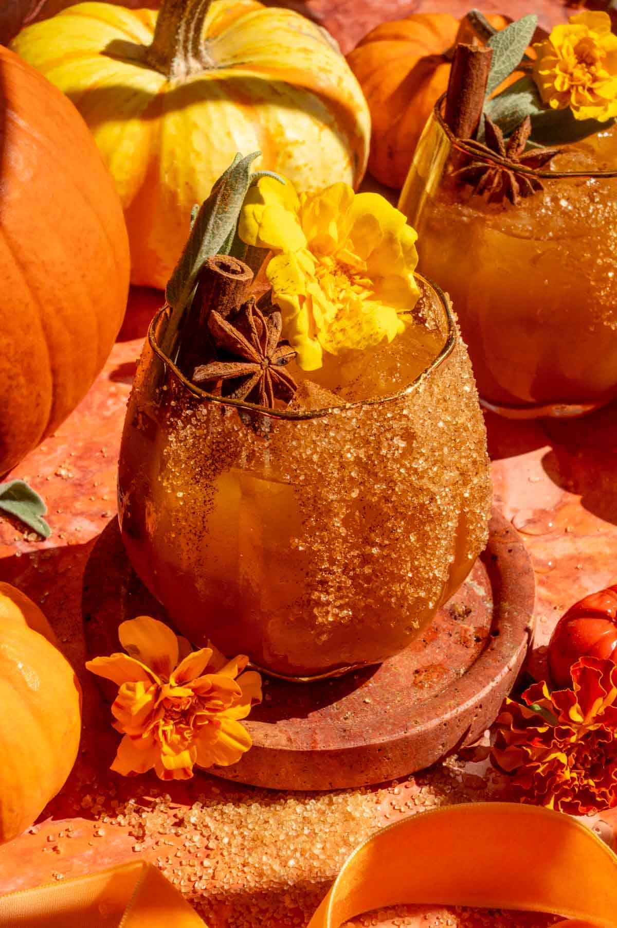 A pumpkin shaped glass fulled with the pumpkin cocktail and garnished with cinnamon, sage, and marigold.