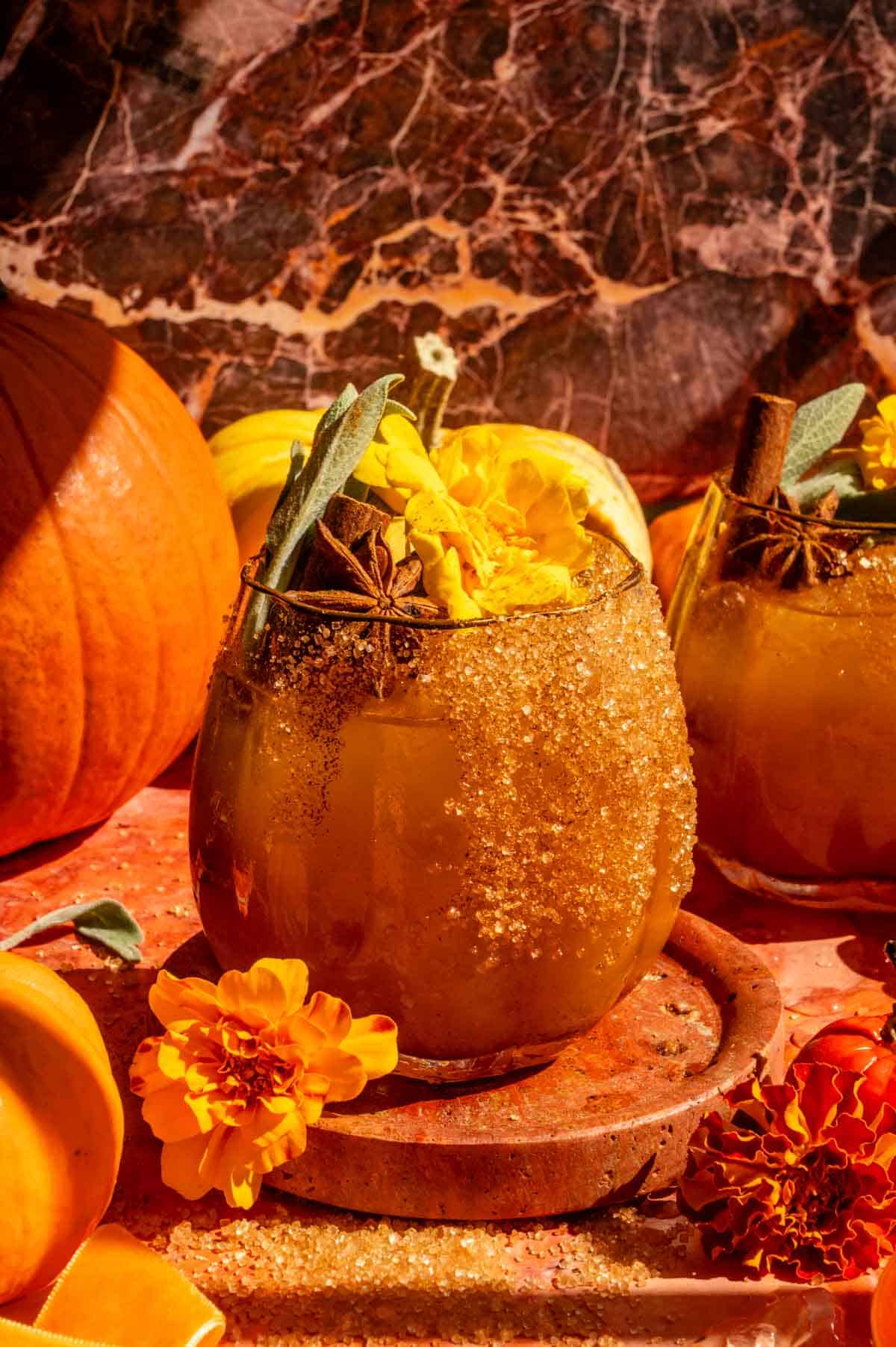 A horizontal shot of A pumpkin shaped glass fulled with the pumpkin cocktail and garnished with cinnamon, sage, and marigold.