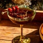 A Manhattan on wood bar cart with a cherry splashing into the drink.