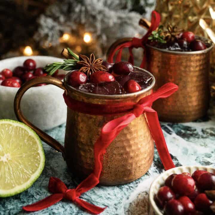 A cranberry mule in a copper cup with a red bow on a green marble table.