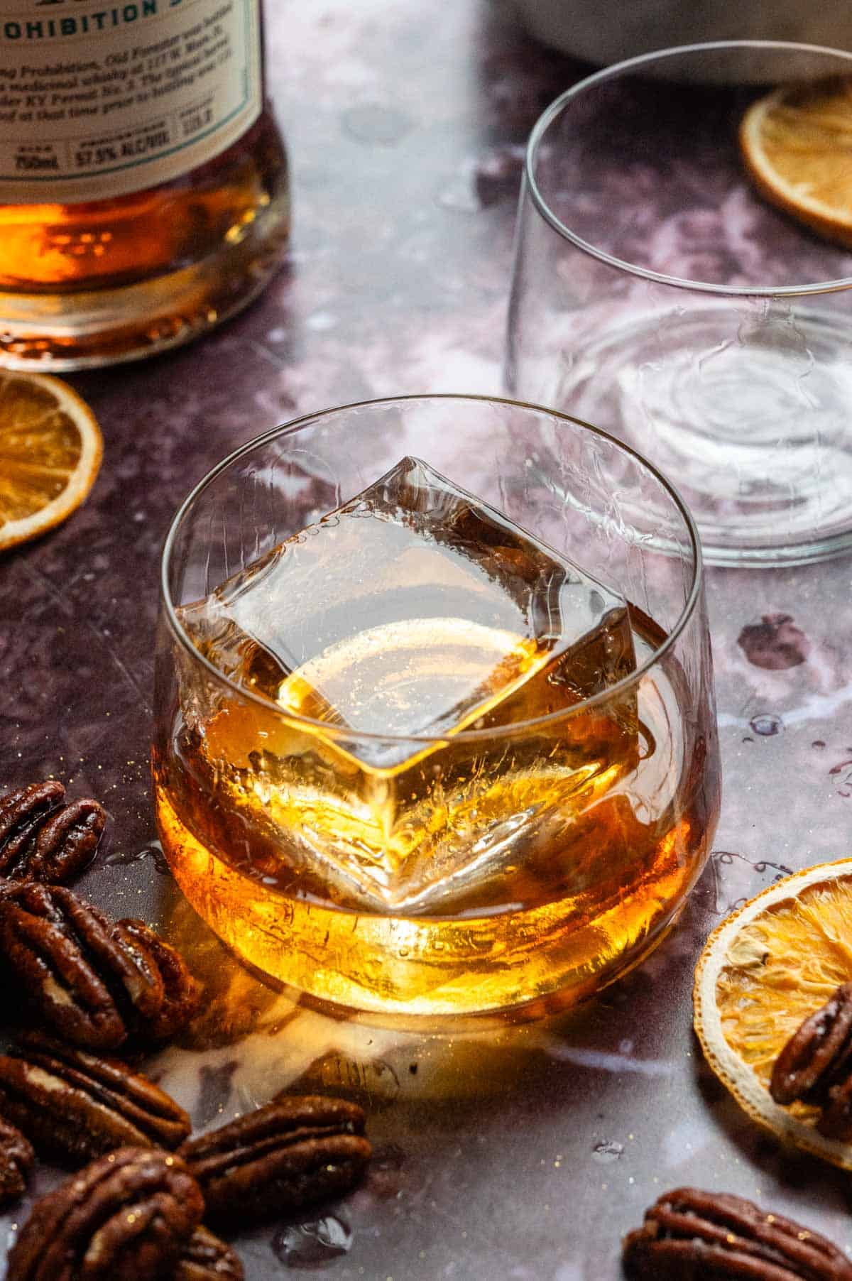 A small old fashioned glass with a large ice cube and 2 ounces of bourbon.