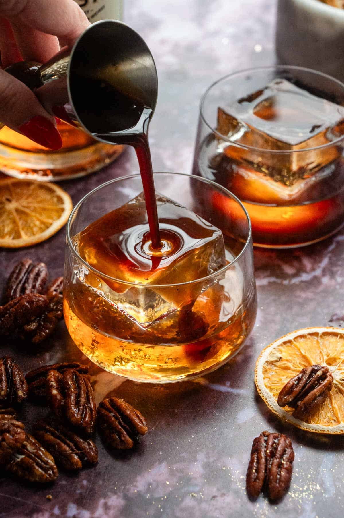 A jigger pouring ½ ounces of syrup over the bourbon.