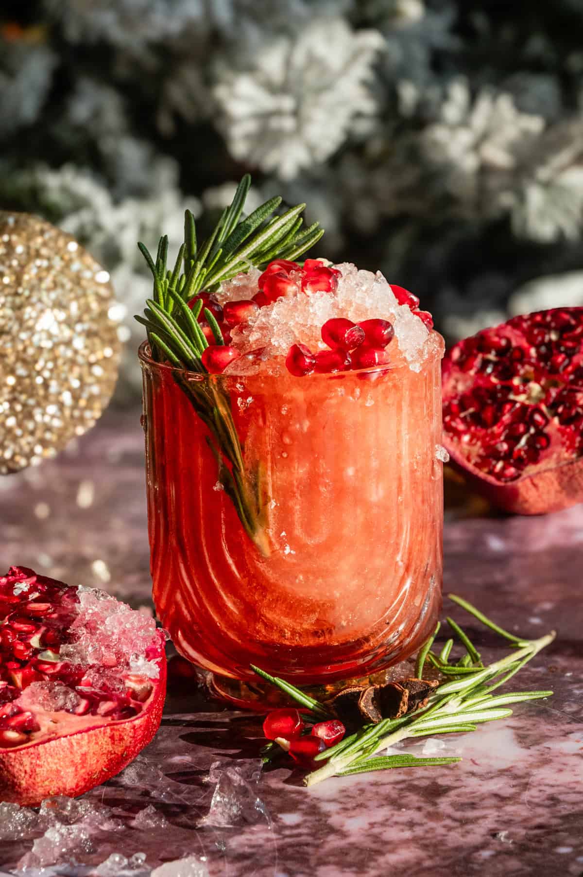 A pomegranate julep filled with fine crushed ice and garnished with rosemary on a purple marble table.