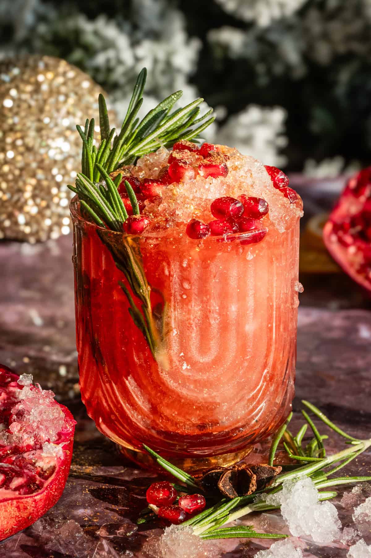 A pomegranate julep filled with fine crushed ice and garnished with rosemary and gold dust on a purple marble table.