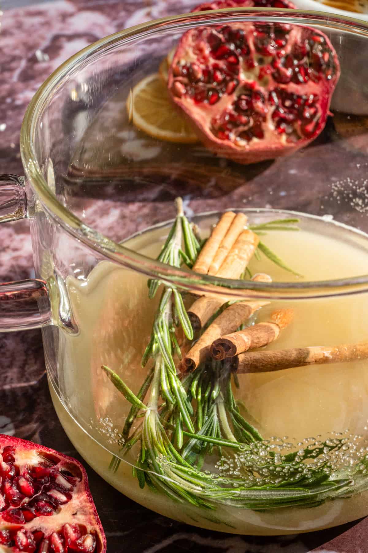 A glass pot willed with water, rosemary, and cinnamon sticks.