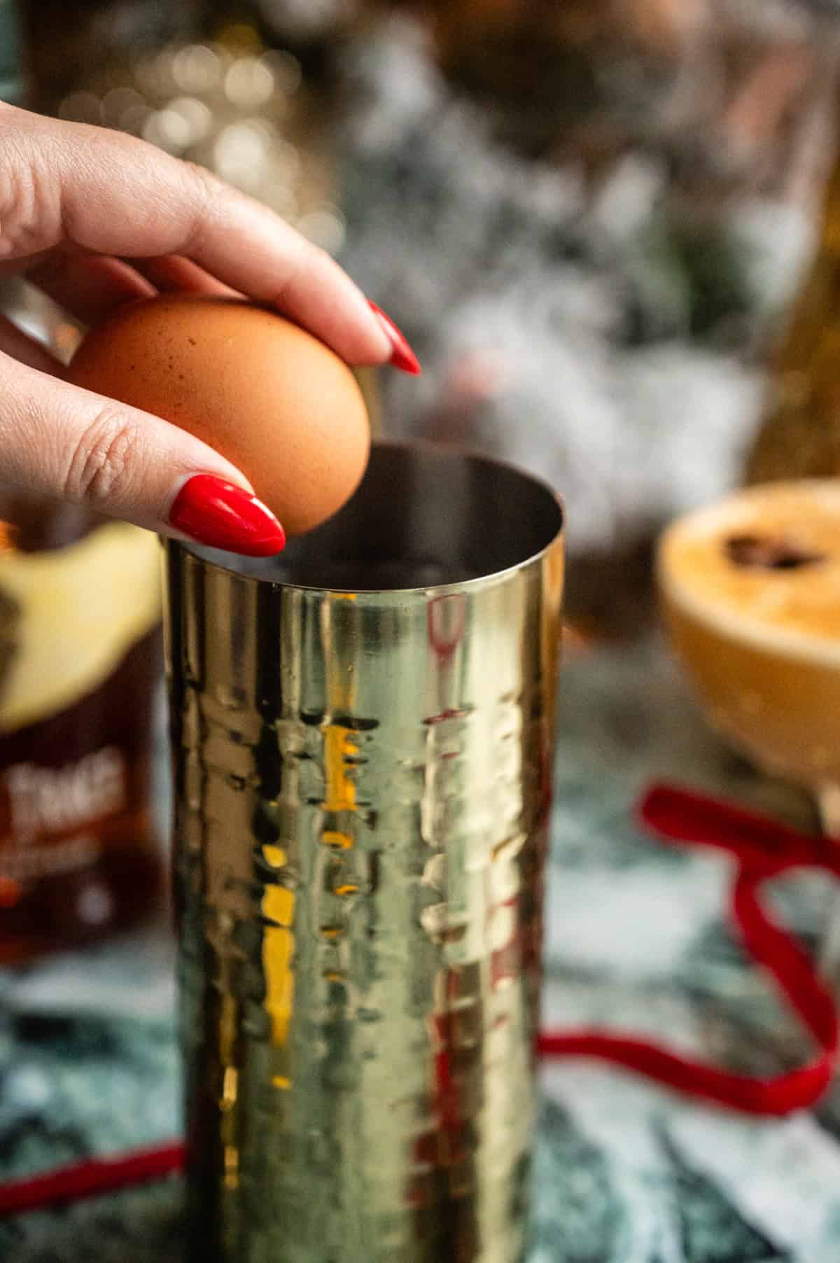 An egg being cracked into the gold cocktail shaker.