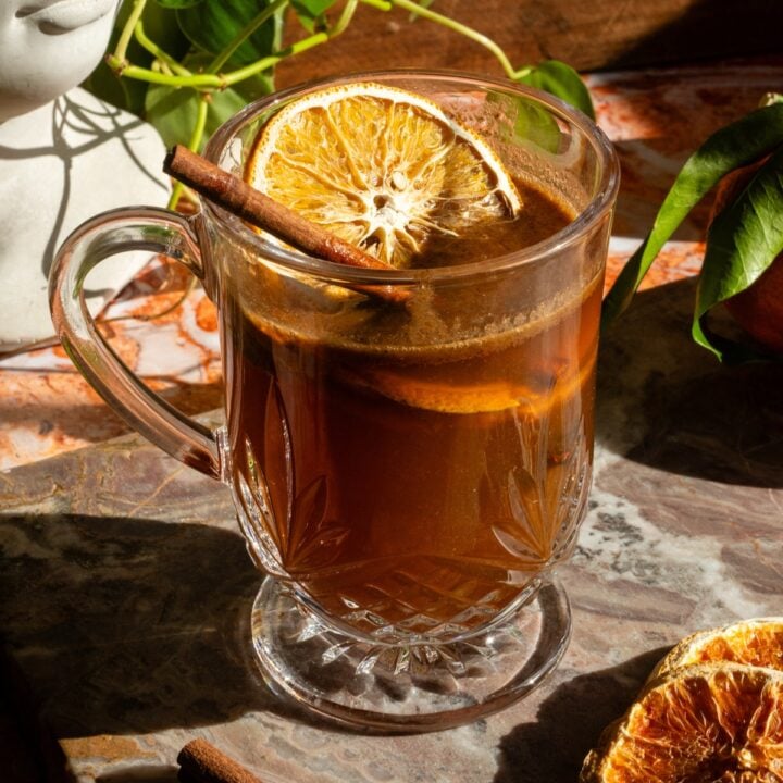 Apple cider hot buttered bourbon in an etched glass mug on a pink marble slab.