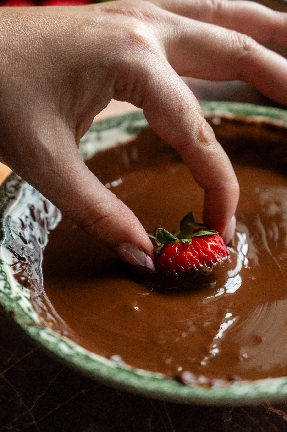 A strawberry being dipped into melted chocolate.