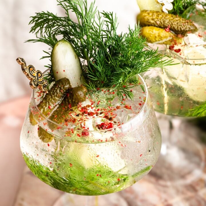 A pickle gin and tonic in a large tonic glass garnished with dill and pickles.