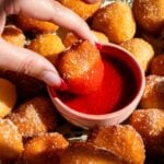 A heart shaped donut hole being dipped in strawberry sauce.