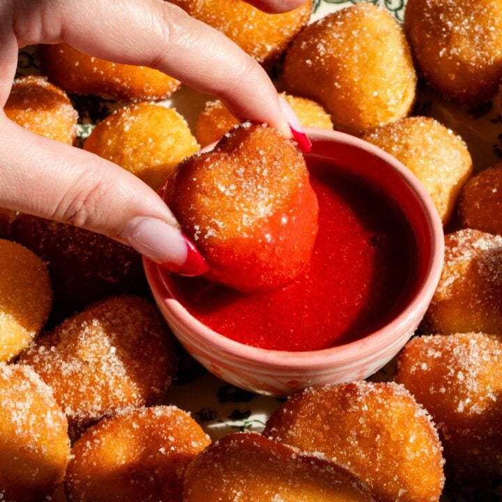 A heart shaped donut hole being dipped in strawberry sauce.