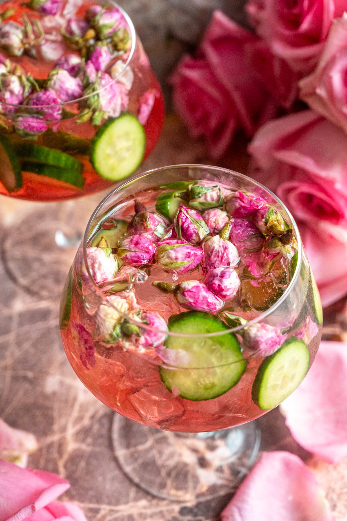 Two glasses of the rose elderflower gin and tonic filled with rose buds on a pink marble table.