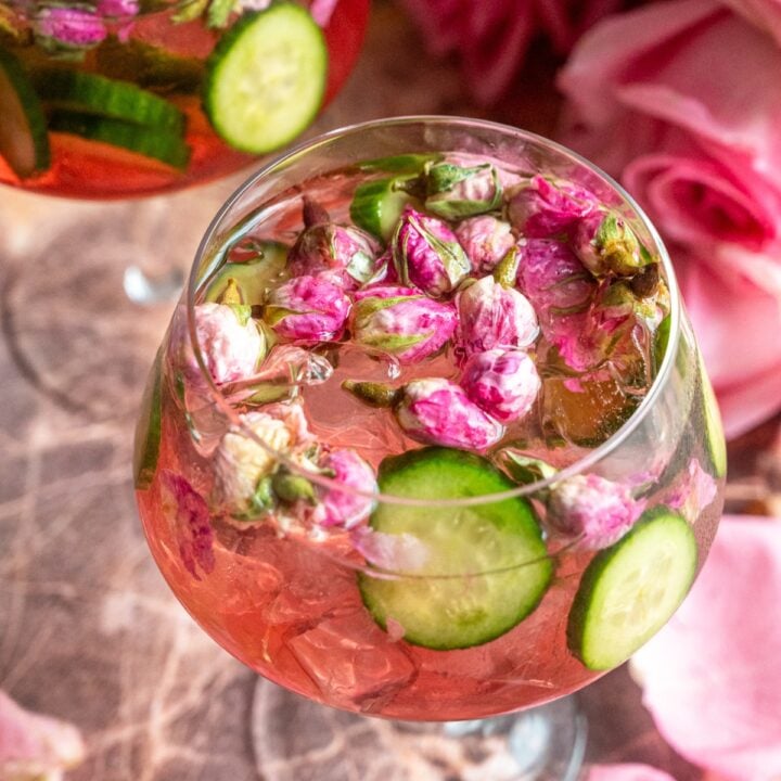 Two glasses of the rose elderflower gin and tonic filled with rose buds on a pink marble table.