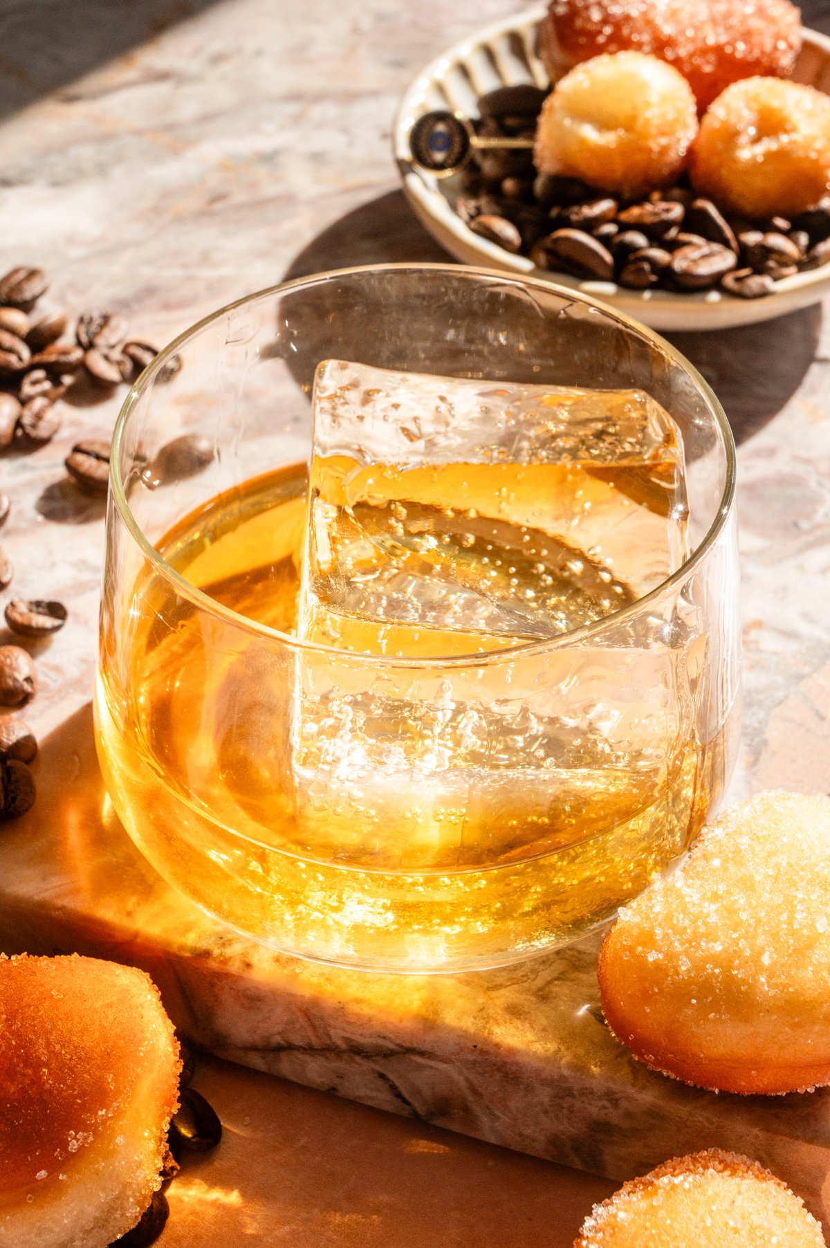 a large clear ice cube and 2 ounces of bourbon sitting in a rocks glass.