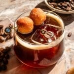 A vanilla espresso old fashioned with two mini donut holes on a pink marble table.