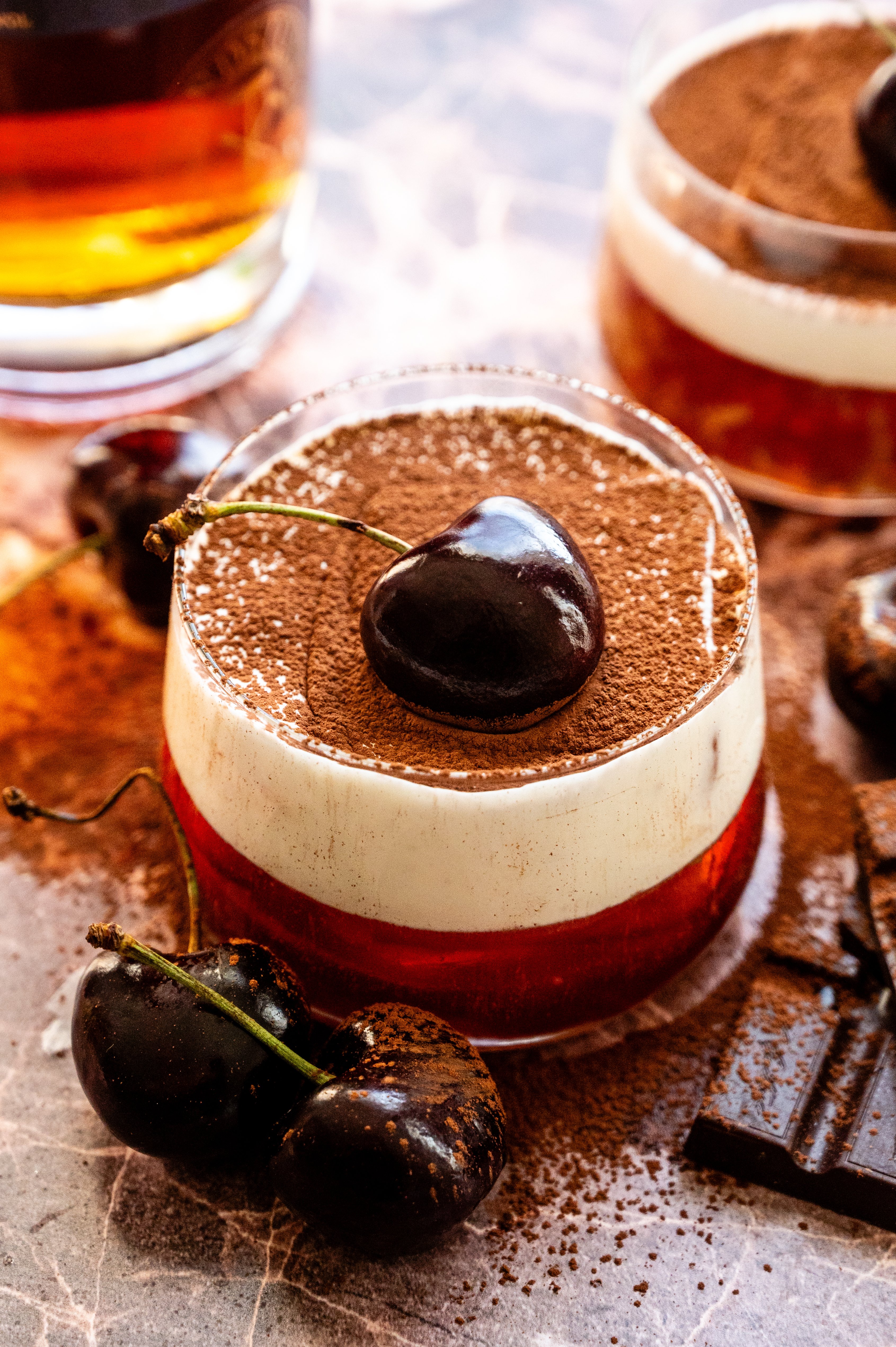 A Black Forest old fashioned on a pink marble table and garnished with a. cherry.