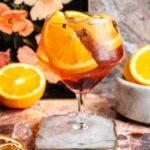 A large ballon glass filled with the Spanish gin and tonic on a pink marble table.