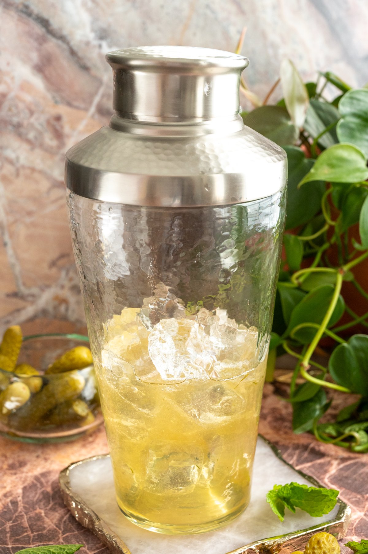 A cocktail shaker filled with the ingredients sitting on a pink marble table.