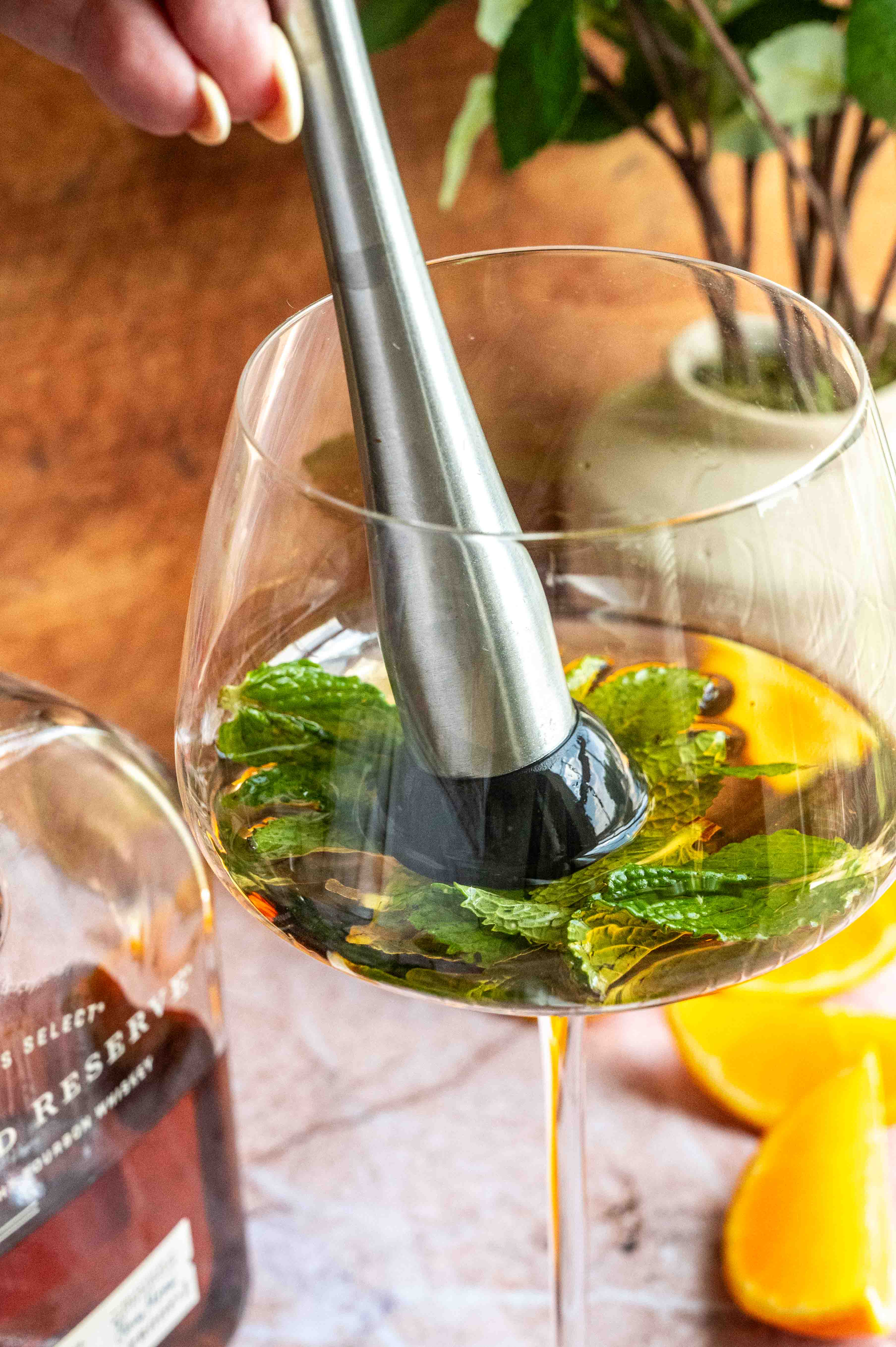 The bourbon, liqueur, and mint being muddled in the stemmed glass.
