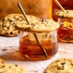 A small old fashioned glass filled with an chocolate chip cookie old fashioned and topped with a chocolate chip cookie with a straw through it.