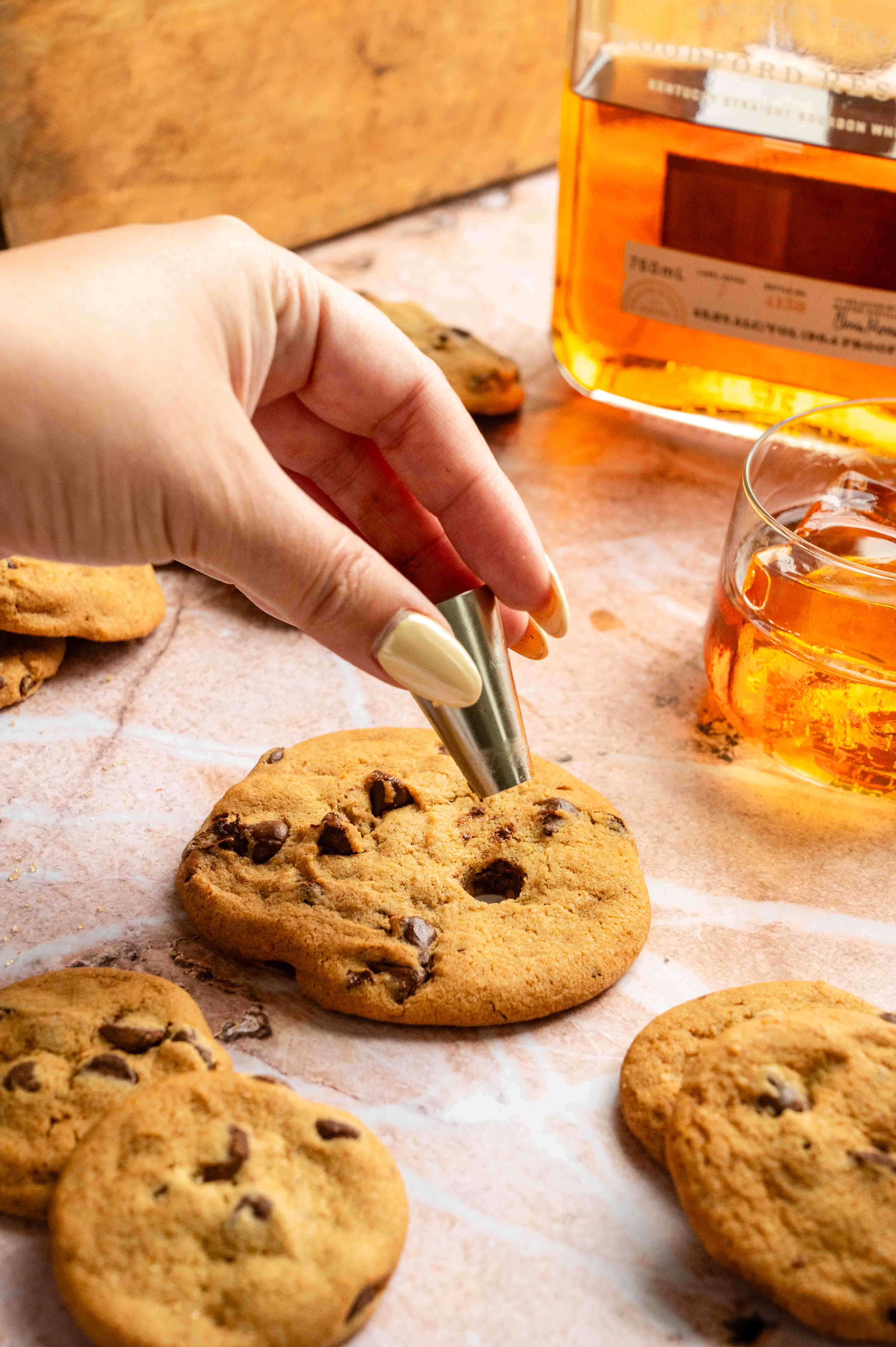 A chocolate chip cookie with a tiny hole being cut out with a piping tip.