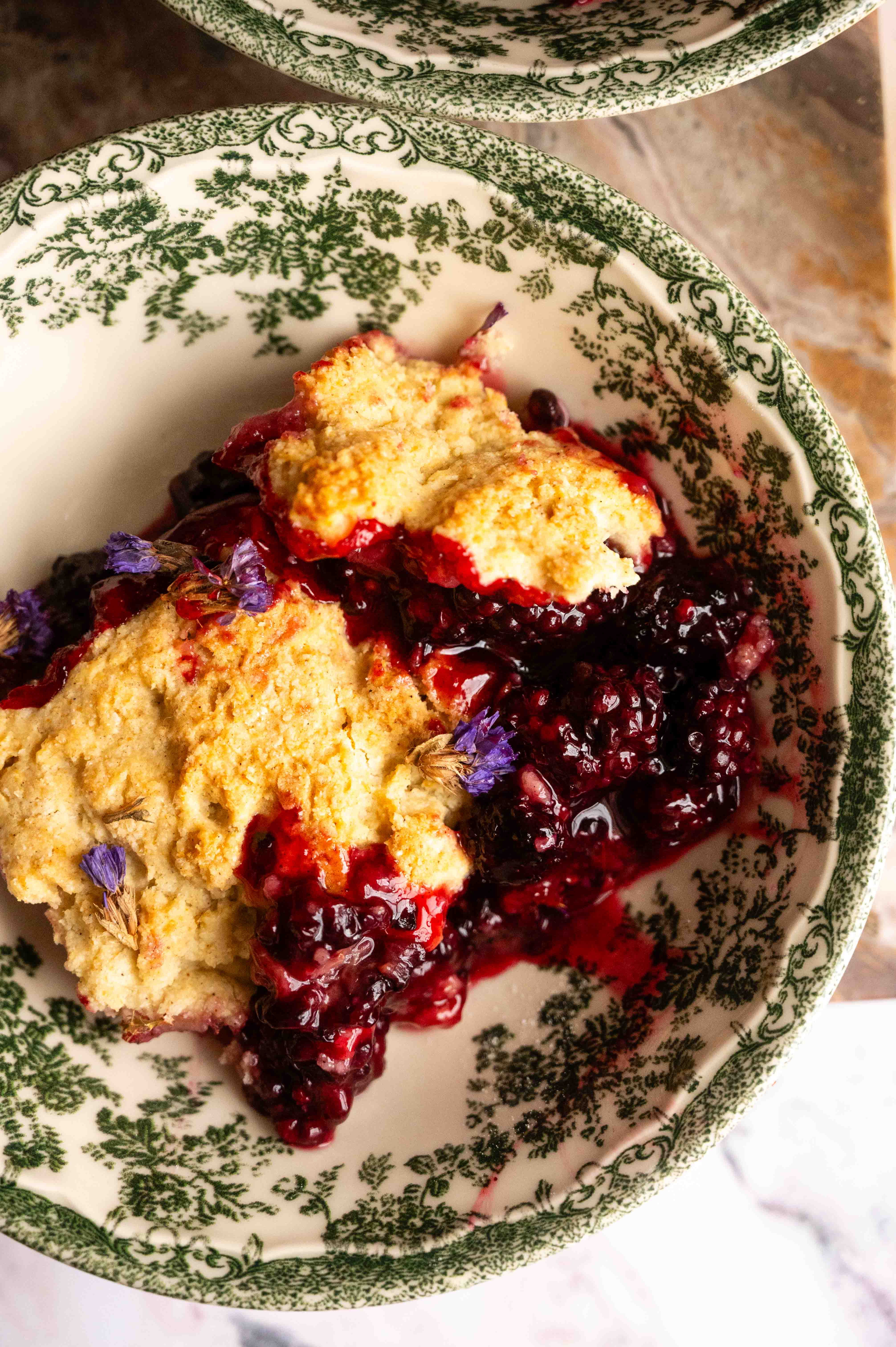 Blackberry cobbler with a biscuit topping in a green floral bowl.