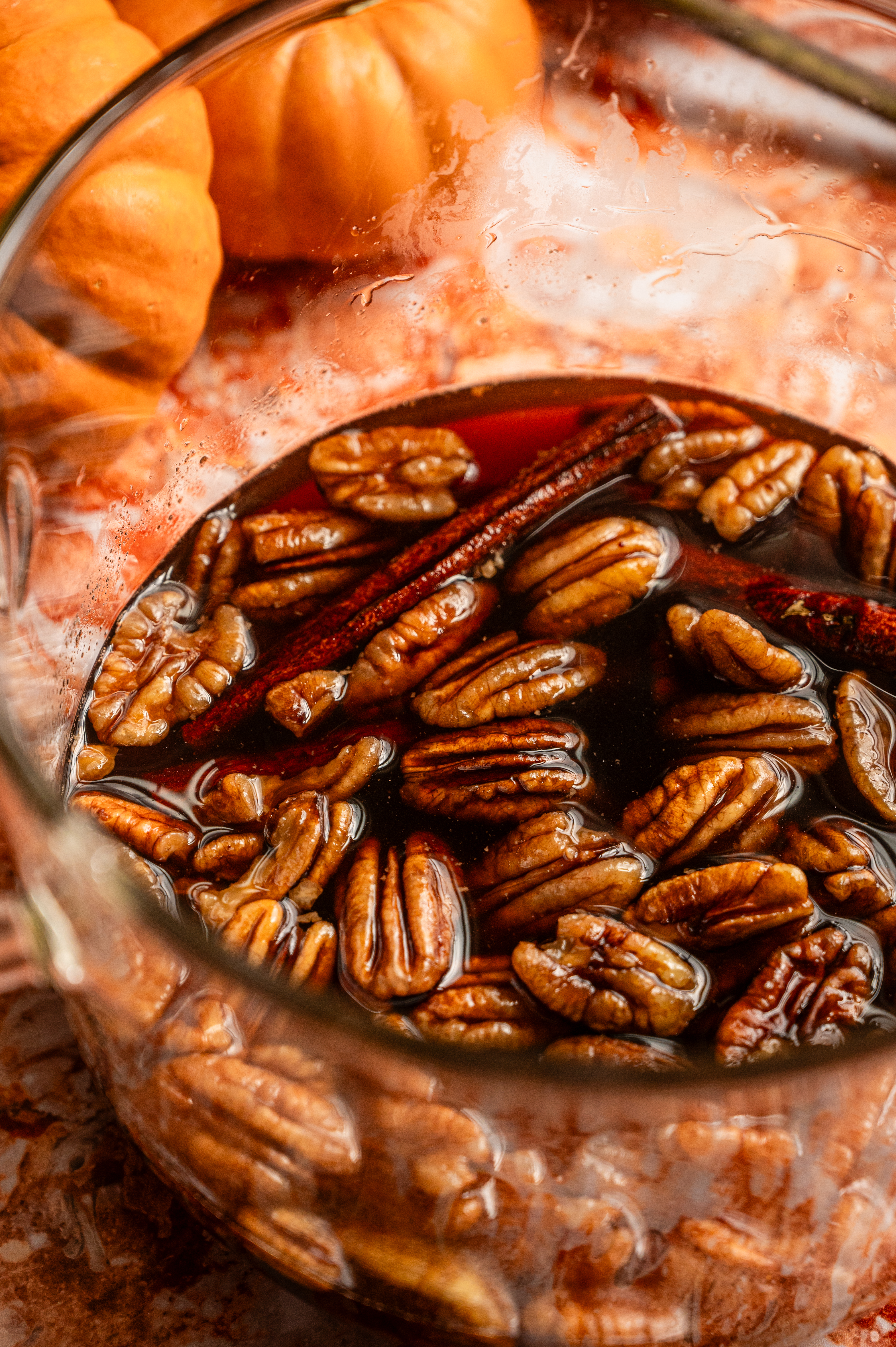 A glass pot with water brown sugar, pecans, and cinnamon sticks.