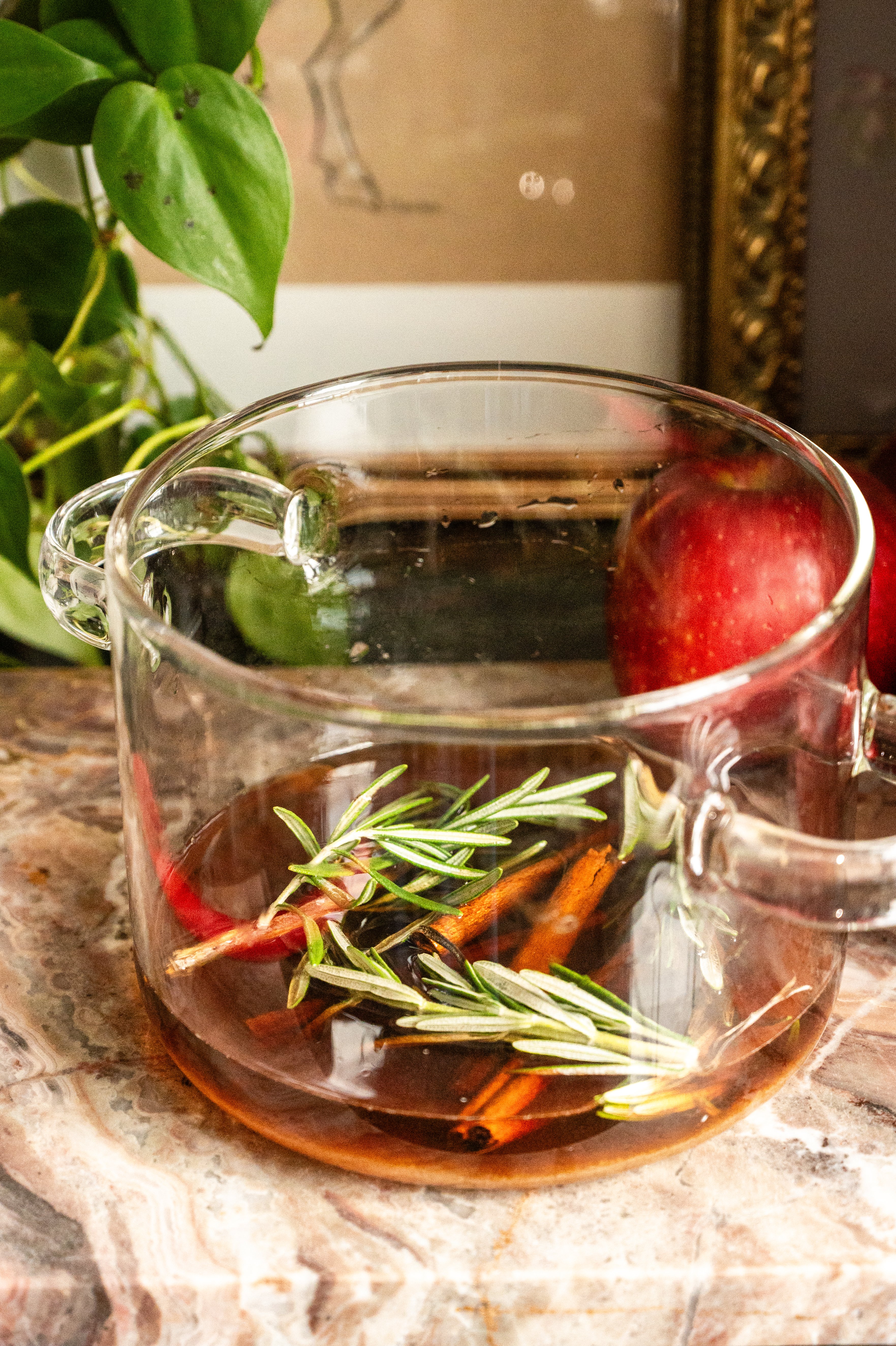 The rosemary simple syrup in a clear pot on a pink marble slab.