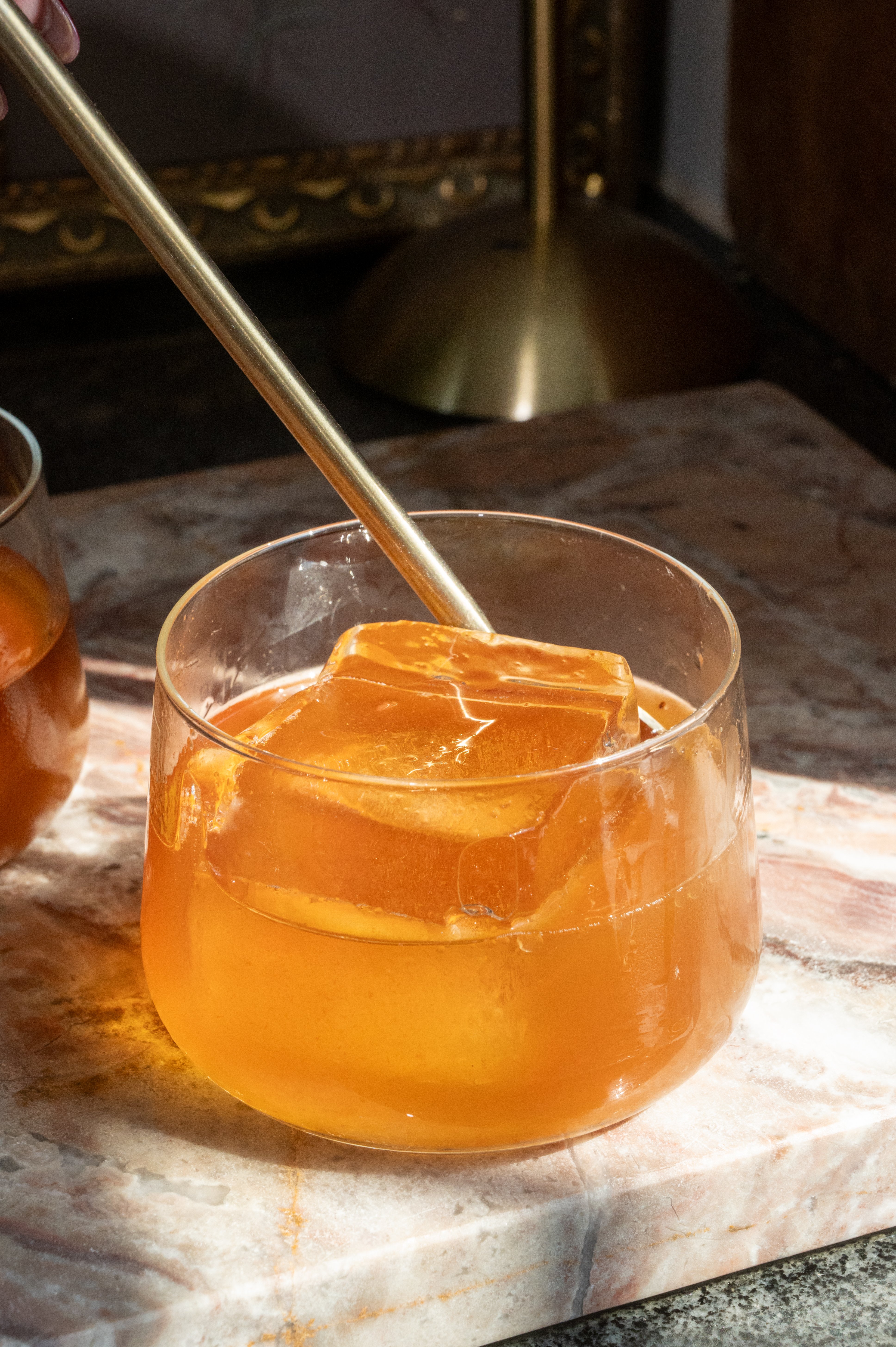 All the ingredients in a rocks glass and being stirred with a bar spoon.