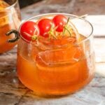 The truffle and tomato old fashioned on a pink marble slab and garnish with 3 cherry tomatoes .